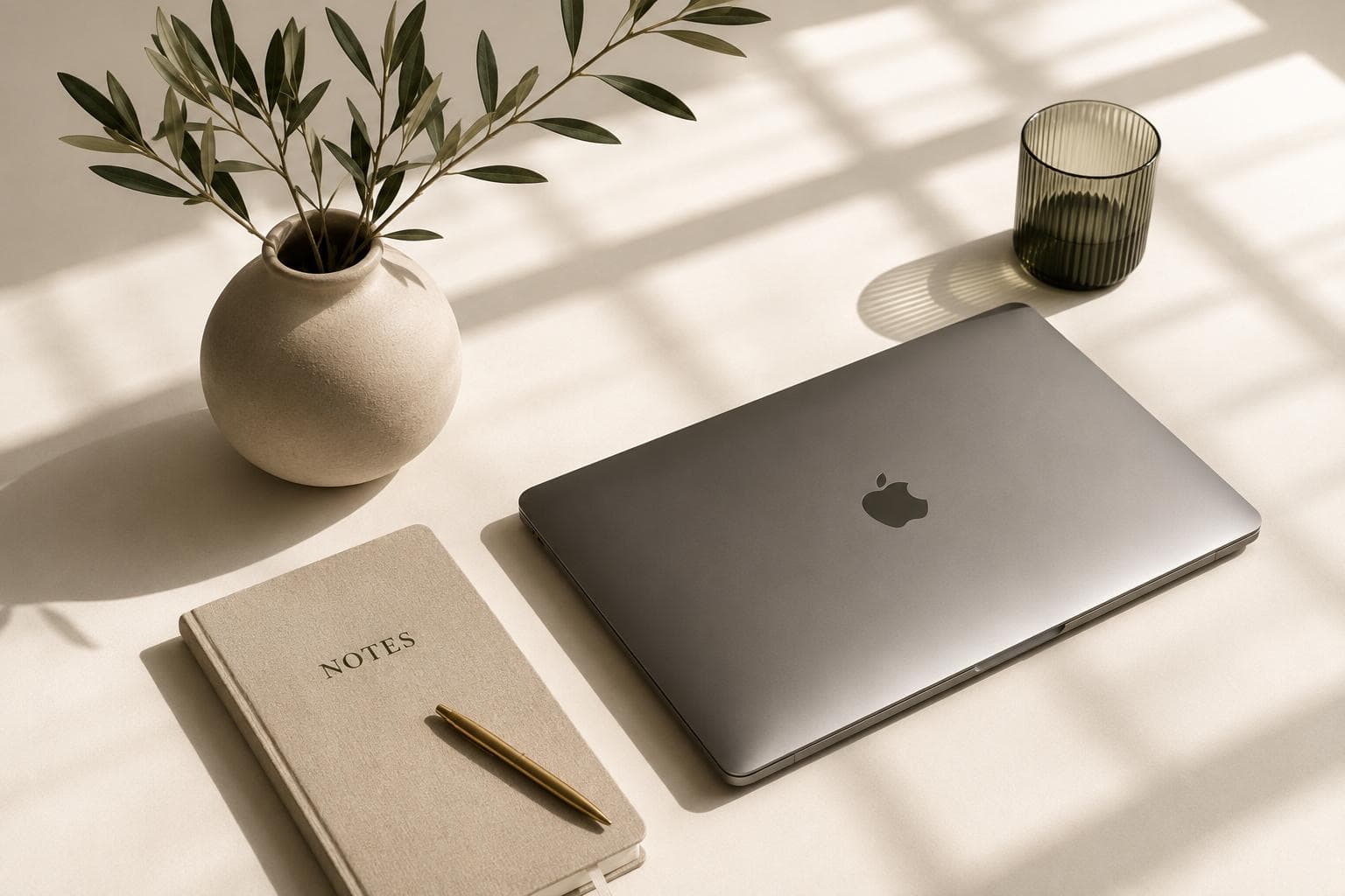 A calm workspace — laptop, linen notebook and an olive branch in soft light