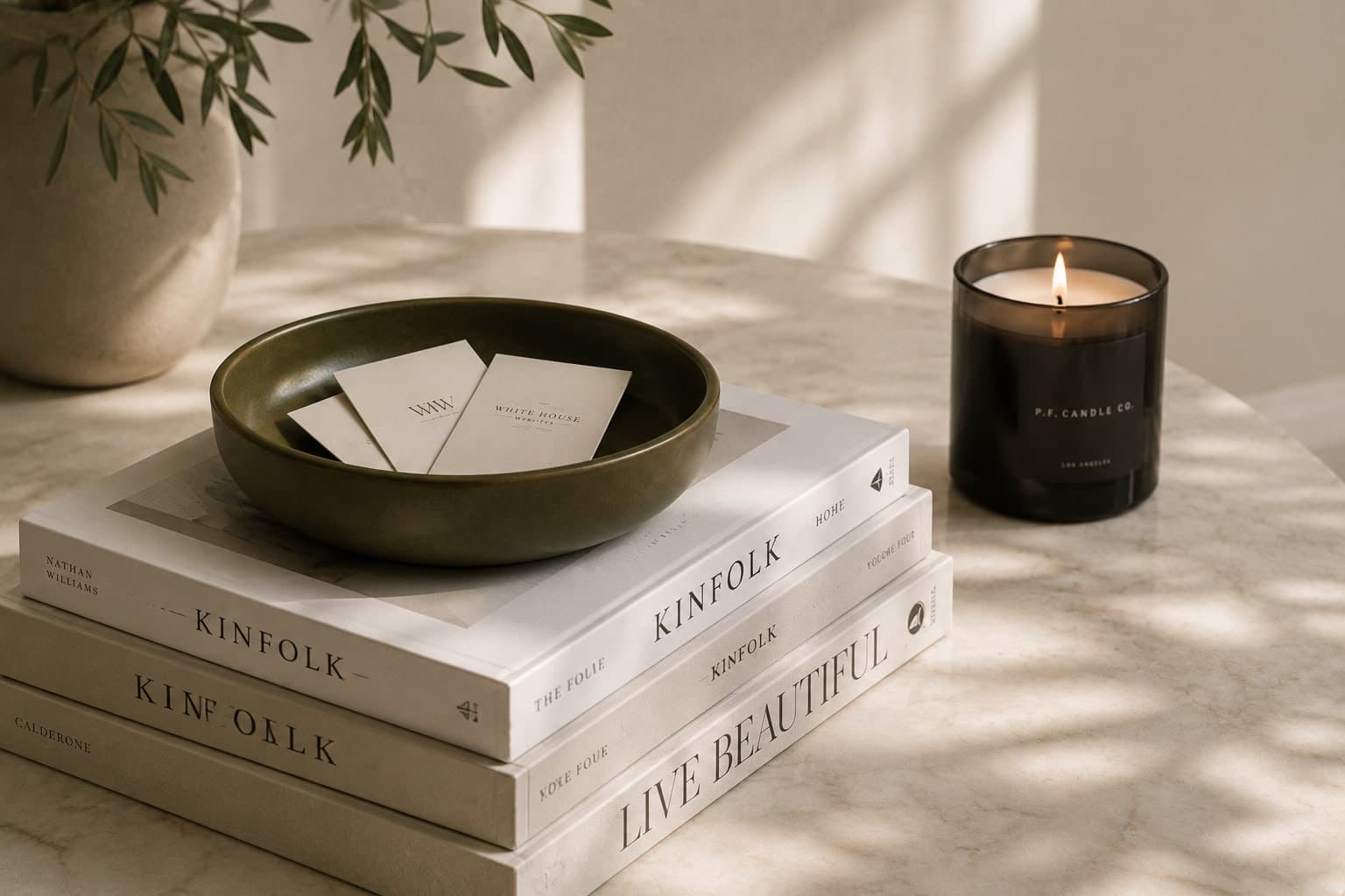 Coffee-table books and business cards in an olive ceramic bowl, candlelight